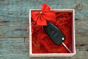 voiture clé dans une cadeau boîte avec une rouge ruban arc sur une en bois Contexte. cadeau pour Noël ou Valentin est journée ou présent un abstrait concept. photo