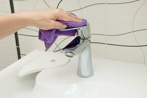 une femme main lavages une robinet avec une chiffon dans le salle de bains photo