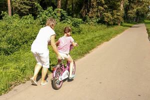 mère enseigne sa petite fille à balade une bicyclette dans le parc sur une ensoleillé journée photo