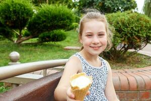 mignonne fille en portant en dehors la glace crème tandis que séance dans le parc sur une banc photo