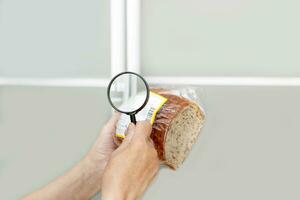 Sénior femme examine le composition de des produits avec une grossissant verre photo