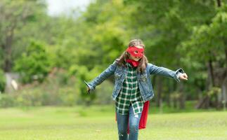 sur une magnifique journée dans le parc, une Jeune fille jouit sa vacances. espiègle avec une rouge super-héros costume et masque. photo