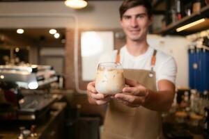 barista en portant une verre de du froid latté café dans le sien mains à client photo