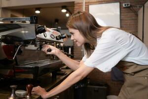 Jeune femelle barista en train de préparer café dans café. femelle barista en utilisant café machine. photo