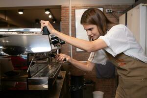 Jeune femelle barista en train de préparer café dans café. femelle barista en utilisant café machine. photo