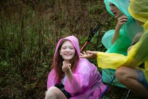 groupe de copains dans imperméable avec sacs à dos randonnée dans le forêt, asseoir et abri de le pluie photo