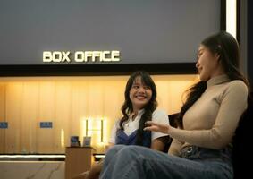 deux Jeune asiatique femmes en mangeant pop corn et attendre pour en train de regarder film à de face de boîte Bureau photo