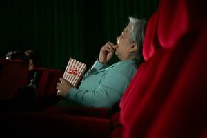 asiatique Sénior femme en train de regarder film à le cinéma dans le soir temps. photo