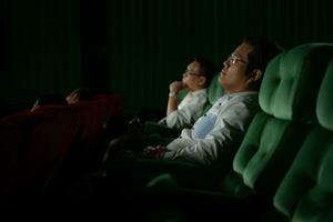 Jeune couple en train de regarder film dans cinéma, séance sur le vert des places. photo