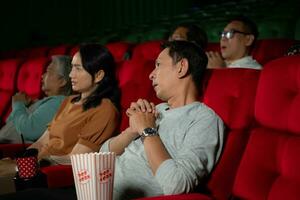 groupe de asiatique Sénior copains en train de regarder comédie film et rire à le cinéma avec pop corn photo