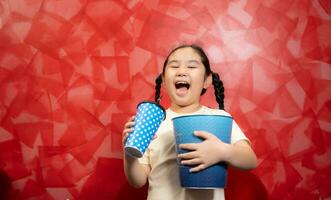 asiatique enfant fille en mangeant pop corn et en buvant un soda sur rouge mur arrière-plan, cinéma concept, photo