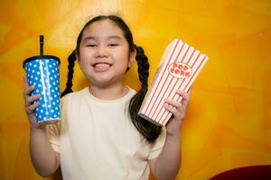 asiatique enfant fille en mangeant pop corn et en buvant un soda sur Jaune mur arrière-plan, cinéma concept, photo