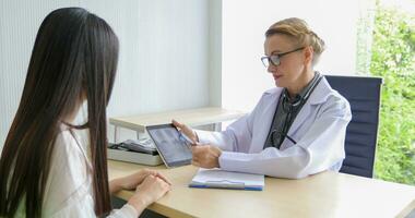 asiatique femme patient séance avec médecin à propos sa maladies et montrant radiographie résultats avec du sang pression et cœur taux la mesure avec stéthoscope photo