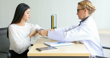 asiatique femme patient séance avec médecin à propos sa maladies et montrant radiographie résultats avec du sang pression et cœur taux la mesure avec stéthoscope photo