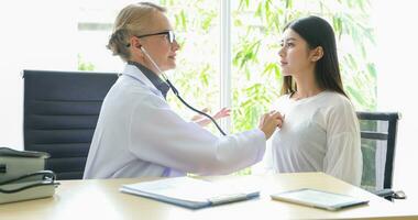 asiatique femme patient séance avec médecin à propos sa maladies et montrant radiographie résultats avec du sang pression et cœur taux la mesure avec stéthoscope photo