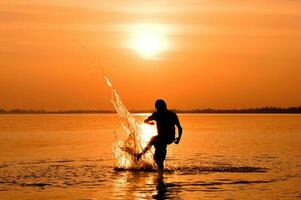 silhouette de garçon en jouant dans le mer à le coucher du soleil photo