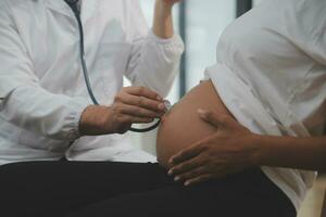 femelle médecin est vérification Enceinte femme avec stéthoscope. concept soins pour Enceinte femme photo