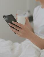 efficace Jeune millénaire fille séance sur une lit dans le matin, les usages portable ordinateur et mange des croissants et les boissons café pour petit déjeuner photo