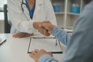 souriant Jeune femelle médecin secouer main proche santé Assurance traiter avec personnes âgées patient à consultation dans hôpital. content femme gp poignée de main salutation avoir connaissance avec mature homme dans clinique. photo