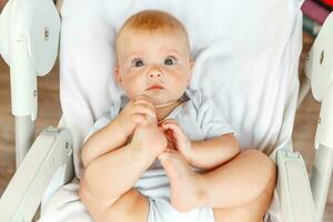 mignonne peu nouveau née fille avec souriant visage à la recherche à caméra sur blanc Contexte. bébé bébé repos en jouant mensonge vers le bas sur alimentation chaise à maison. maternité content enfant concept. photo