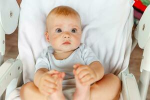 mignonne peu nouveau née fille avec souriant visage à la recherche à caméra sur blanc Contexte. bébé bébé repos en jouant mensonge vers le bas sur alimentation chaise à maison. maternité content enfant concept. photo