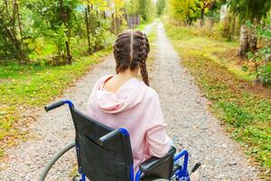 jeune femme handicapée heureuse en fauteuil roulant sur la route dans le parc de l'hôpital en attente de services aux patients. fille paralysée dans une chaise invalide pour personnes handicapées en plein air dans la nature. notion de réhabilitation. photo