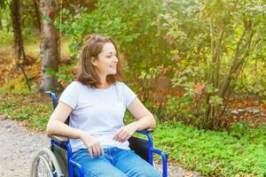 jeune femme handicapée heureuse en fauteuil roulant sur la route dans le parc de l'hôpital en attente de services aux patients. fille paralysée dans une chaise invalide pour personnes handicapées en plein air dans la nature. notion de réhabilitation. photo