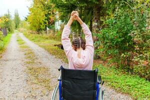 jeune femme handicapée heureuse en fauteuil roulant sur la route dans le parc de l'hôpital en profitant de la liberté. fille paralysée dans une chaise invalide pour personnes handicapées en plein air dans la nature. notion de réhabilitation. photo