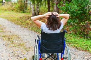 jeune femme handicapée heureuse en fauteuil roulant sur la route dans le parc de l'hôpital en profitant de la liberté. fille paralysée dans une chaise invalide pour personnes handicapées en plein air dans la nature. notion de réhabilitation. photo