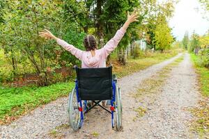 jeune femme handicapée heureuse en fauteuil roulant sur la route dans le parc de l'hôpital en profitant de la liberté. fille paralysée dans une chaise invalide pour personnes handicapées en plein air dans la nature. notion de réhabilitation. photo