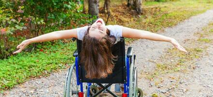 jeune femme handicapée heureuse en fauteuil roulant sur la route dans le parc de l'hôpital en profitant de la liberté. fille paralysée dans une chaise invalide pour personnes handicapées en plein air dans la nature. notion de réhabilitation. photo