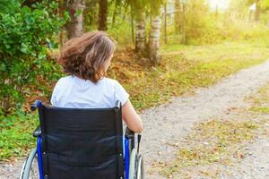 jeune femme handicapée heureuse en fauteuil roulant sur la route dans le parc de l'hôpital en profitant de la liberté. fille paralysée dans une chaise invalide pour personnes handicapées en plein air dans la nature. notion de réhabilitation. photo