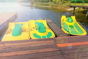 Station de pédalos ou pédalos catamarans. vélos à eau jaune verrouillés au quai du quai de la marina du lac le jour d'été ensoleillé. activité de loisirs d'été à l'extérieur. photo