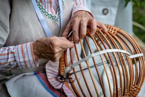 une vieille femme en costume national fait un panier en osier local. photo