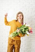 femme en vêtements jaunes tenant un bouquet de tulipes et une carte vierge photo