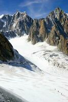 deux gens sont randonnée en haut une Montagne avec neige couvert montagnes photo