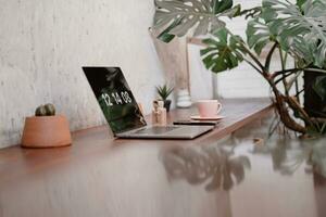une portable sur le table avec une tasse de café avec monstera feuille photo