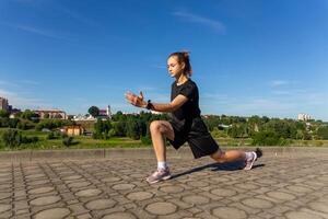 jeune, en forme et sportif fille dans noir vêtements élongation après le faire des exercices dans le Urbain ville parc. photo