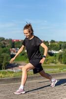 jeune, en forme et sportif fille dans noir vêtements élongation après le faire des exercices dans le Urbain ville parc. photo