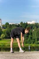 jeune, en forme et sportif fille dans noir vêtements élongation après le faire des exercices dans le Urbain ville parc. photo