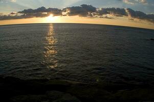 une bateau est voile à travers le océan à le coucher du soleil photo