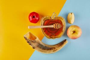 rosh hashanah - juif Nouveau année vacances concept. bol dans le forme de un Pomme avec Miel, pommes, grenades, shofar sur jaune-bleu Contexte photo
