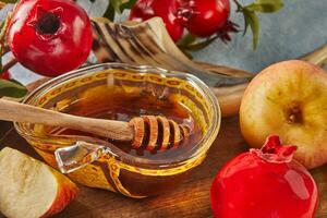 rosh hashanah - juif Nouveau année vacances concept. bol dans le forme de un Pomme avec Miel, pommes, grenades, shofar sur une bleu Contexte photo