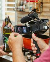 elles ou ils sont tournage vidéo de cuisson, bouteille de olive pétrole dans le mains de le cuisinier photo