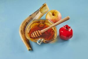 rosh hashanah - juif Nouveau année vacances concept. bol dans le forme de un Pomme avec Miel, pommes, grenades, shofar sur une bleu Contexte photo