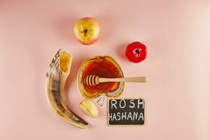 rosh hashanah caractères - juif Nouveau année vacances concept. bol dans le forme de un Pomme avec Miel, pommes, grenades, shofar sur rose Contexte. photo