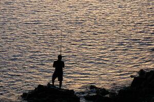 homme rétro-éclairé avec une pêche barre dans le mer photo