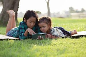 deux Jeune les filles mensonge sur le pelouse à la recherche à leur Téléphone (s, été, d'or heure, le coucher du soleil. sstkhome photo