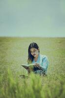 une la personne séance sur le herbe en train de lire une livre, attrayant gens séance sur le herbe en train de lire une livre, une fille en train de lire une livre dans le champ photo