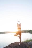 jeune femme en bonne santé pratique le yoga au lac de montagne pendant le coucher du soleil. photo